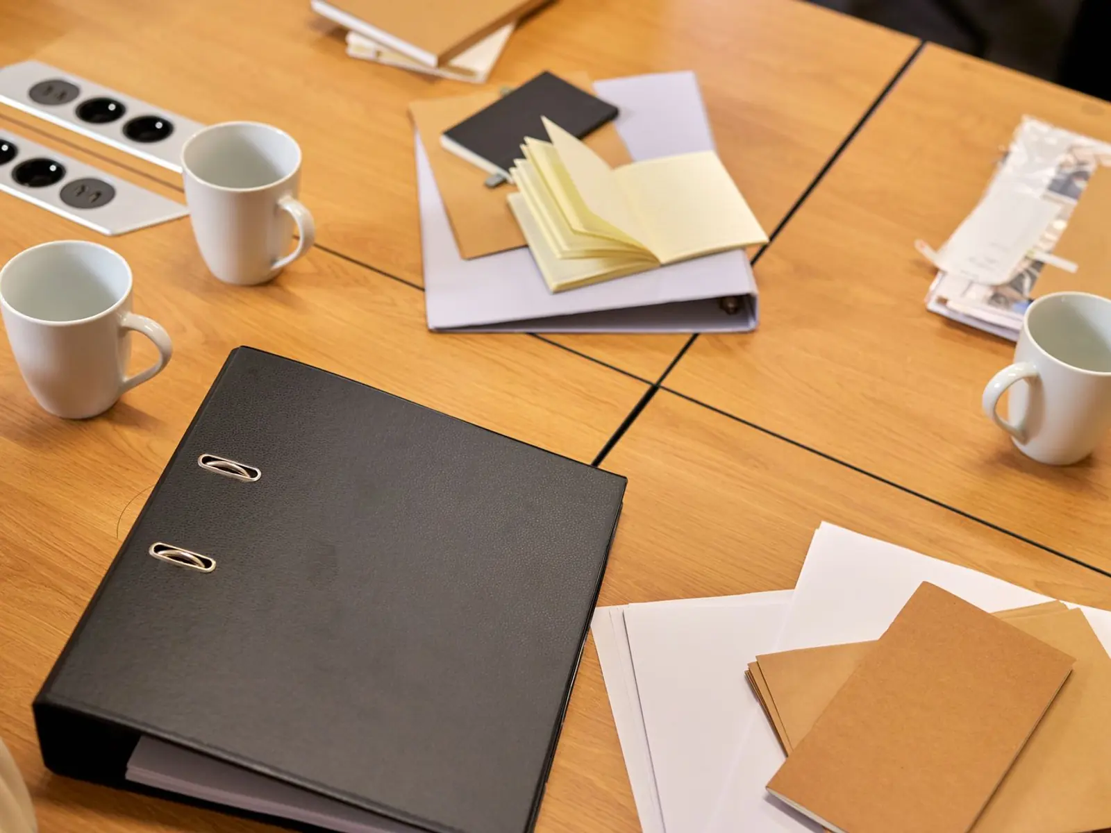 Mesa de reuniones de madera con archivadores, cuadernos y tazas de café