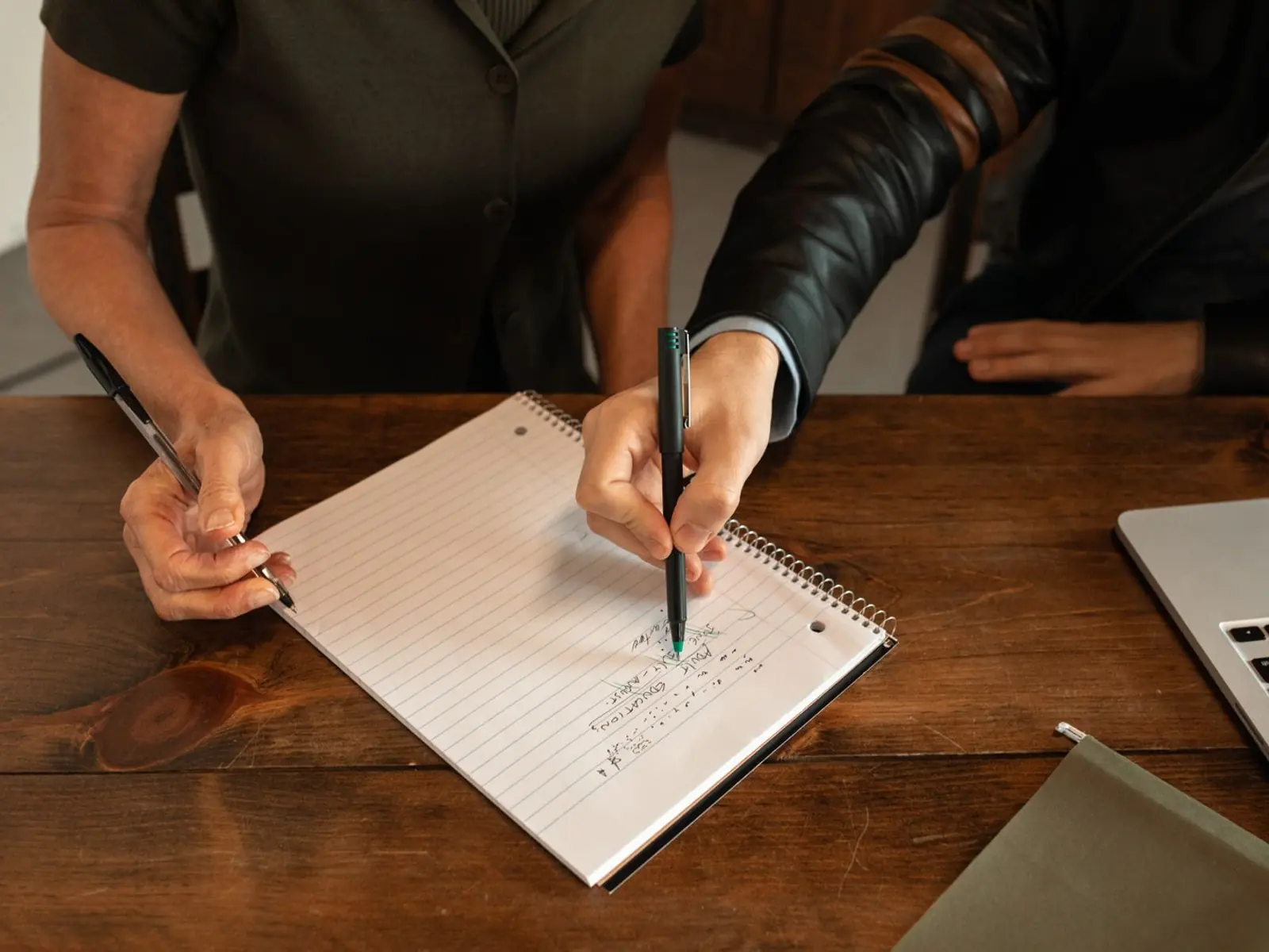 Dos personas tomando notas en un cuaderno sobre la mesa de un despacho