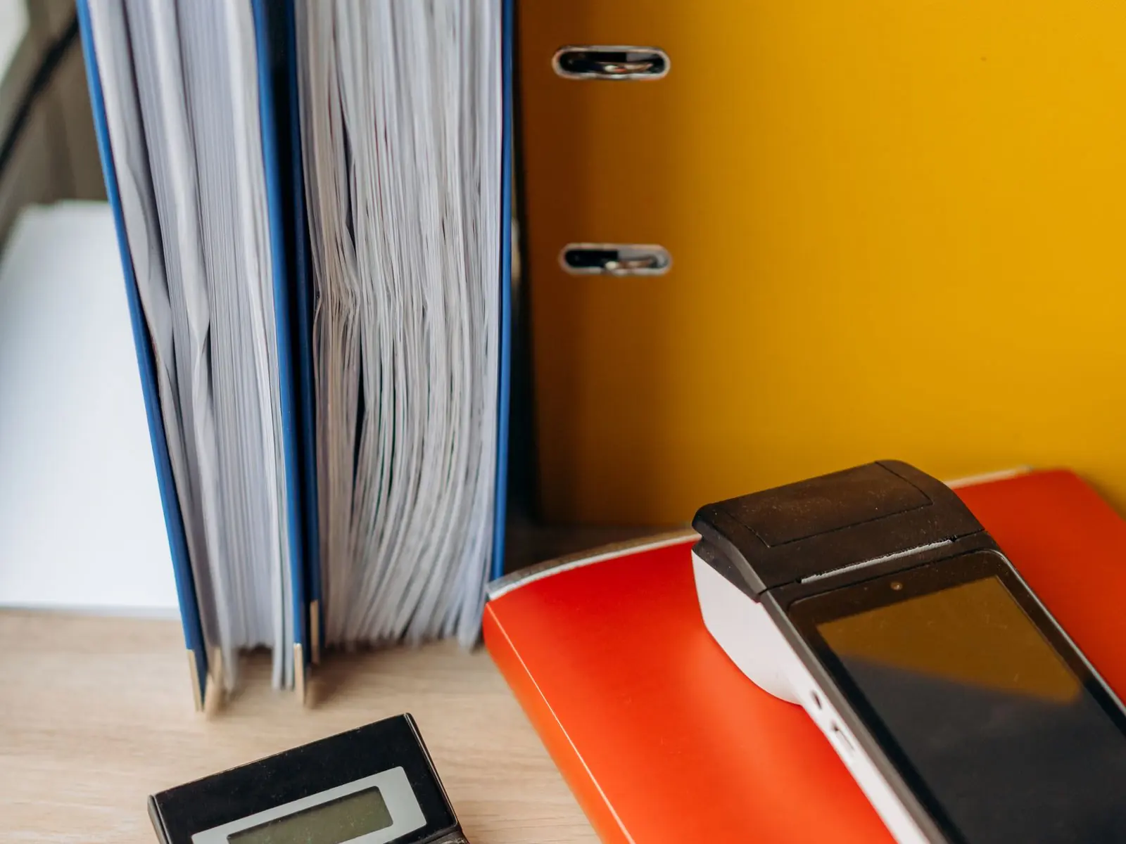 Archivadores llenos de documentos junto a una calculadora en la mesa de una asesoría